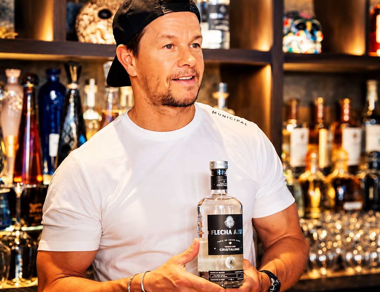 A guest holding a bottle at an upscale bar lit by warm backlit shelves